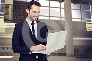 Composite image of smiling businessman standing and using laptop