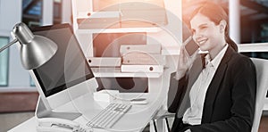 Composite image of smiling businesswoman talking on mobile phone at desk with computer