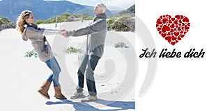 Composite image of smiling couple spinning on the beach in warm clothing