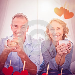 Composite image of smiling middle aged couple sitting on the couch having coffee