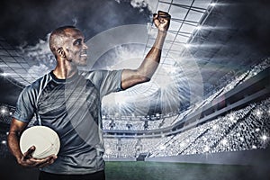 Composite image of sportsman with clenched fist holding rugby ball after victory