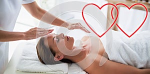 Composite image of therapist performing reiki on woman love hearts