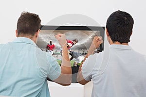 Composite image of two excited soccer fans watching tv