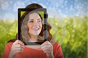 Composite image of woman holding digital tablet in front of her face