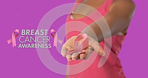 Composite image of woman showing breast cancer ribbon against purple background