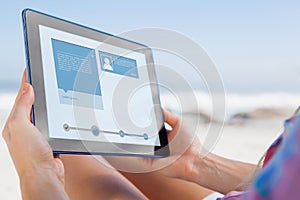 Composite image of woman sitting on beach in deck chair using tablet pc