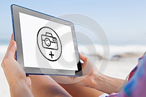 Composite image of woman sitting on beach in deck chair using tablet pc