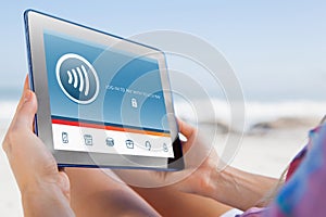 Composite image of woman sitting on beach in deck chair using tablet pc