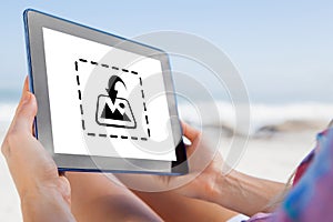 Composite image of woman sitting on beach in deck chair using tablet pc