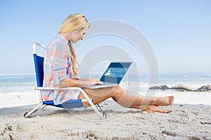 Composite image of woman sitting on beach using her laptop