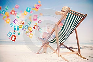 Composite image of woman in sunhat sitting on beach in deck chair using tablet pc