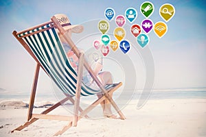 Composite image of woman in sunhat sitting on beach in deck chair using tablet pc