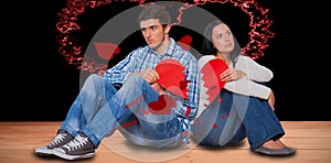 Composite image of young couple sitting on floor with broken heart