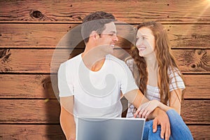 Composite image of young couple sitting on floor using laptop