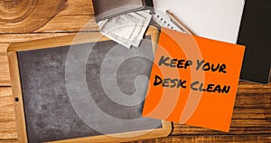 Composite of keep your desk clean on sticky note with slate, notepad, pen and wallet with currency