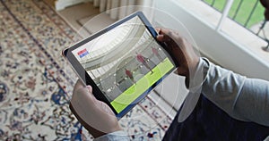 Composite of man sitting at home watching rugby match on tablet