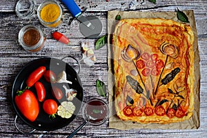 Composition of appetizing vegetable pizza, metal plate with tomatoes, pepper and garlic, spice jars and basil leaves on a wooden