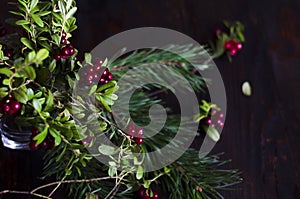 Composition of autumn forest plants, branches with red lingonberry berries, spruce and pine branch on a dark wooden background.