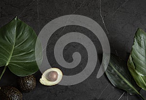 Composition with avocado and tropical leaves on a black marble surface top view