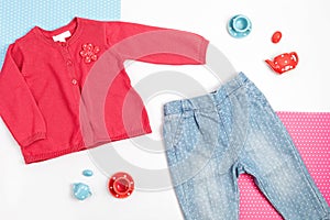 Composition with baby red cardigan, jeans, and toy tea set on blue, pink, and white background