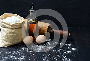 Composition of bag of wheat flour, eggs, oil and rolling pin. Preparation for kneading dough, baking on dark background. Space for