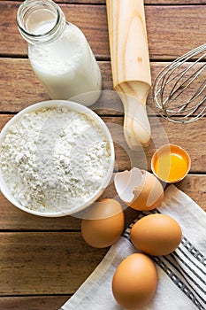 Composition from baking ingredients. Eggs cracked shell bright yellow yolk. Milk in glass bottle flour arranged on table