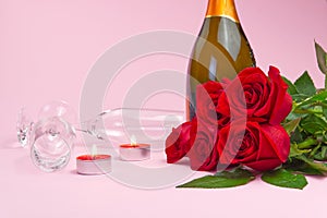 A composition of a beautiful bouquet of roses, candles, glasses and a bottle of champagne creates a romantic card. The concept of