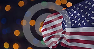 Composition of billowing american flag over orange, blue and green bokeh lights on dark background