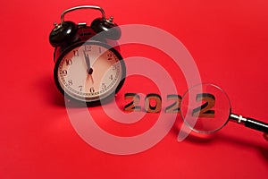 Composition with black alarm clock with midnight on the clock face and cropped hand holding magnifying glass showing number two of