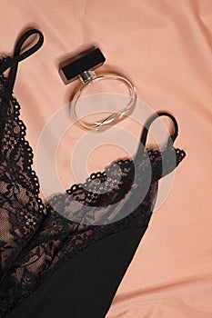 The composition of the black lace negligee and a bottle of perfume on a pastel silk background.