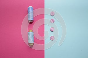 Composition with blue threads and sewing accessories on pink background.
