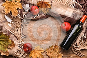 Composition with bottle of wine, warm plaid and autumn leaves on wooden background