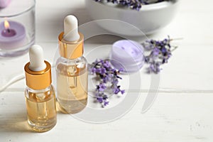 Composition with bottles of essential oil and lavender flowers on white wooden table. Space for text