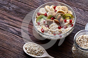 Composition with bowl of oatmeal porrige and dry oatmeal in glassware on vintage wooden table, selective focus