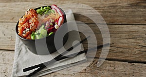 Composition of bowl of rice, salmon and vegetables with chopsticks on wooden background