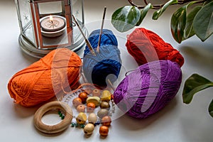 Composition in bright colors of yarn, beads, pins and knitting needles. Nearby is a candle in a metal candlestick and green leaves