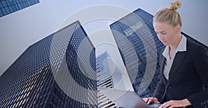 Composition of businesswoman using laptop over modern skyscrappers photo