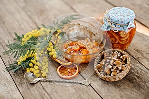 Composition of the candied orange spiral peel with sugar syrup in a glass jar and plate near the saucer with walnuts