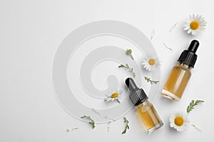 Composition with chamomile flowers and cosmetic bottles of essential oil on white background