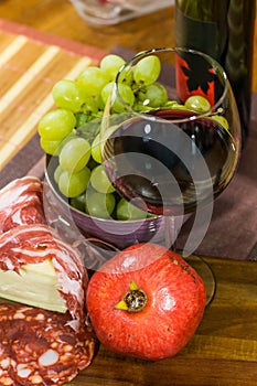 Composition of cheese, bacon, pomegranate, glass of wine and yellow muscat grape on a wooden board