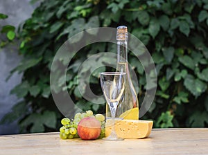 Composition of cheese, grapes, peaches, white , bottles and glasses wine on a wooden round table. in the courtyard.