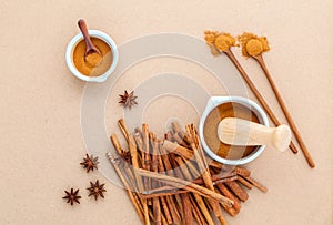 Composition of cinnamon stick and cinnamon powder in white mortar with star anise and wooden spoon on brown background .