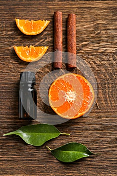 Composition with citrus essential oil, cinnamon sticks and orange slices on wooden table, top view