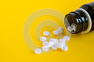 Composition close up white pills with bottle on yellow background with blank space for text.