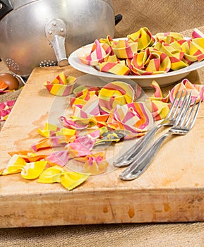 Composition of colorful ravioli pasta, white plate, two forks and a strainer on a canvas