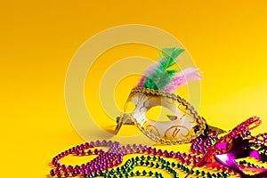 Composition of colourful mardi gras beads and carnival masks on yellow background with copy space