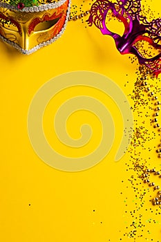 Composition of colourful mardi gras beads and carnival masks on yellow background with copy space