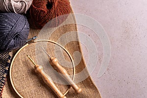 Composition with copy space of punch needle tools on a concrete surface. A jute fabric in an embroidery hoop and needles