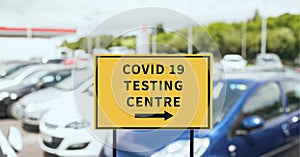 Composition of covid 19 testing centre text on sign over cars in car park
