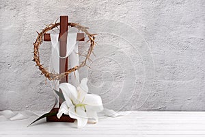 Composition with crown of thorns, wooden cross and lily on light background